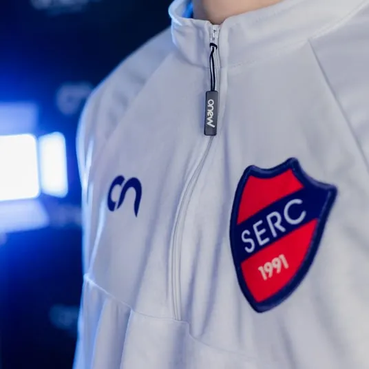 Detalhe de jaqueta branca com escudo bordado e zíper Onew